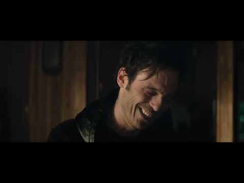 Killing Them Softly official trailer frame: Jackie Cogan in a rain-streaked car, jaw set, city lights smeared outside