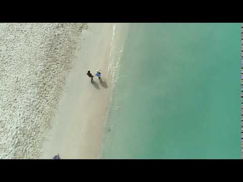 couple walks tropical beach waves aerial drone shot