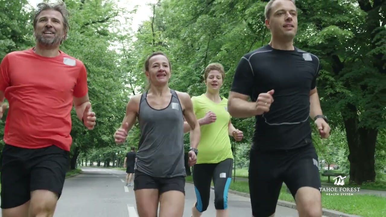 Four runners jogging on a road with green trees behind them