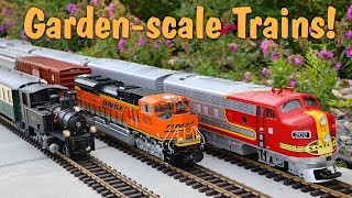 A Steam Train and Two Diesel Model Trains Running Outdoors On A Huge Outdoor Model Train Layout