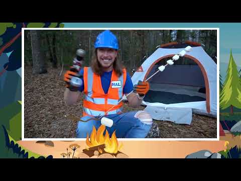 Man in a blue hard hat and orange safety vest sits by a camping tent in a forest, roasting marshmallows over a small fire.