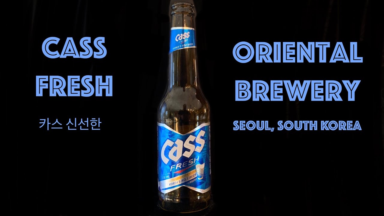 A bottle of Korean Cass Fresh beer with the green glass bottle and silver label held up for a beer review showing the lager's golden color