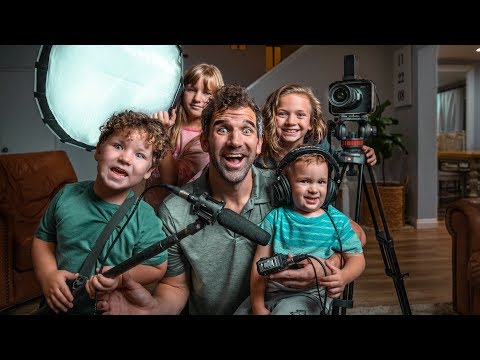 Man and four children posing with a home video setup: camera on a tripod, boom mic, headphones, and a large soft light panel nearby.