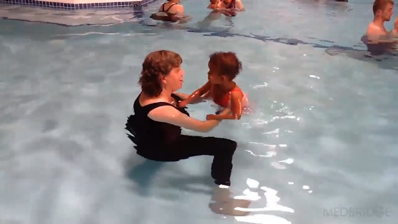 A Medbridge caregiver supports a young swimmer in a lively pool setting.