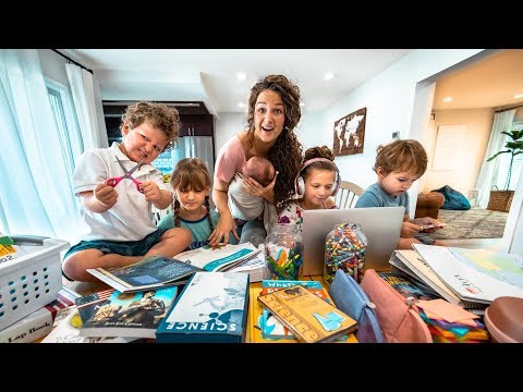 Mother with several children doing homework at a cluttered home table, surrounded by books, crayons, and a laptop in a cozy learning space.