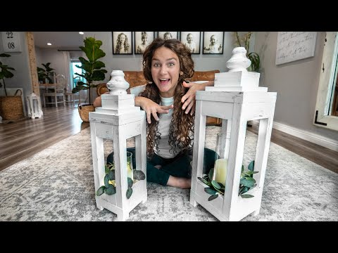 Girl sits cross-legged on a rug between two white wooden lanterns with candles and greenery, smiling excitedly.