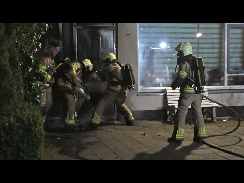 Brandweer ramt met bijl, deurram en halligan tool aangestoken deur in brand open in Zwolle