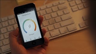 temperature smart app on smartphone screen held above a computer keyboard