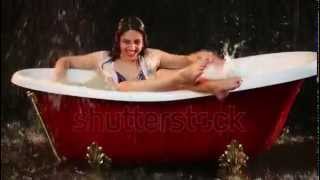 Beautiful girl sitting in the bath and claps her hands over the surface of the water   stock