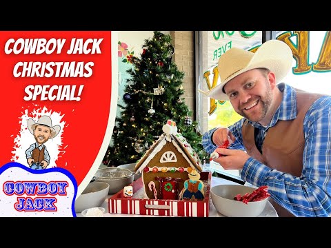 Smiling man in a cowboy hat and vest decorates a gingerbread house at a festive table, with a Christmas tree in the background.