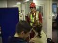 Fall arrest harness being put onto mannequin man by member of the public at a Safety clothing and PPE exhibition by ARCO at family open day at BAE (British Aerospace Engineering) systems in Rochester #8 (flash)