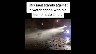 Man stands against water cannon with homemade shield
