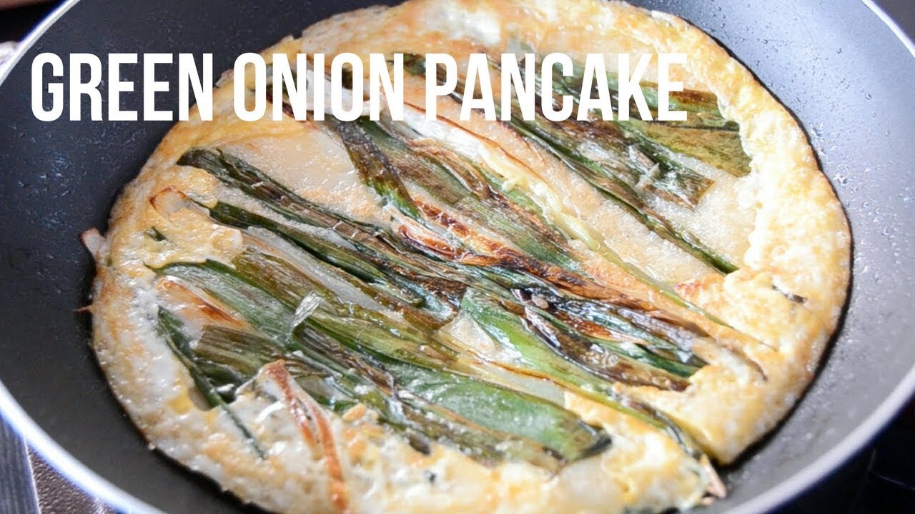 Korean pajeon scallion pancake cooking in a pan with green onions visible through the batter