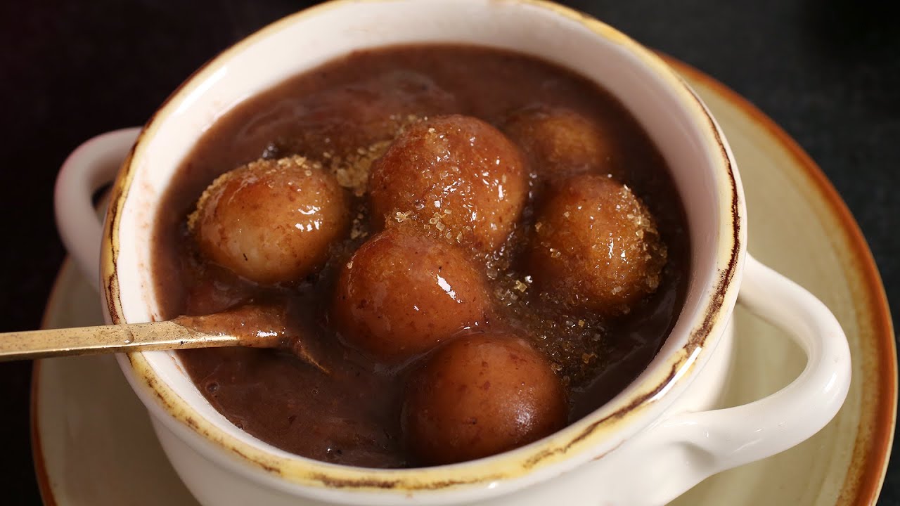 A bowl of Korean patjuk red bean porridge with chewy white rice flour dumplings floating in the thick reddish-brown bean puree
