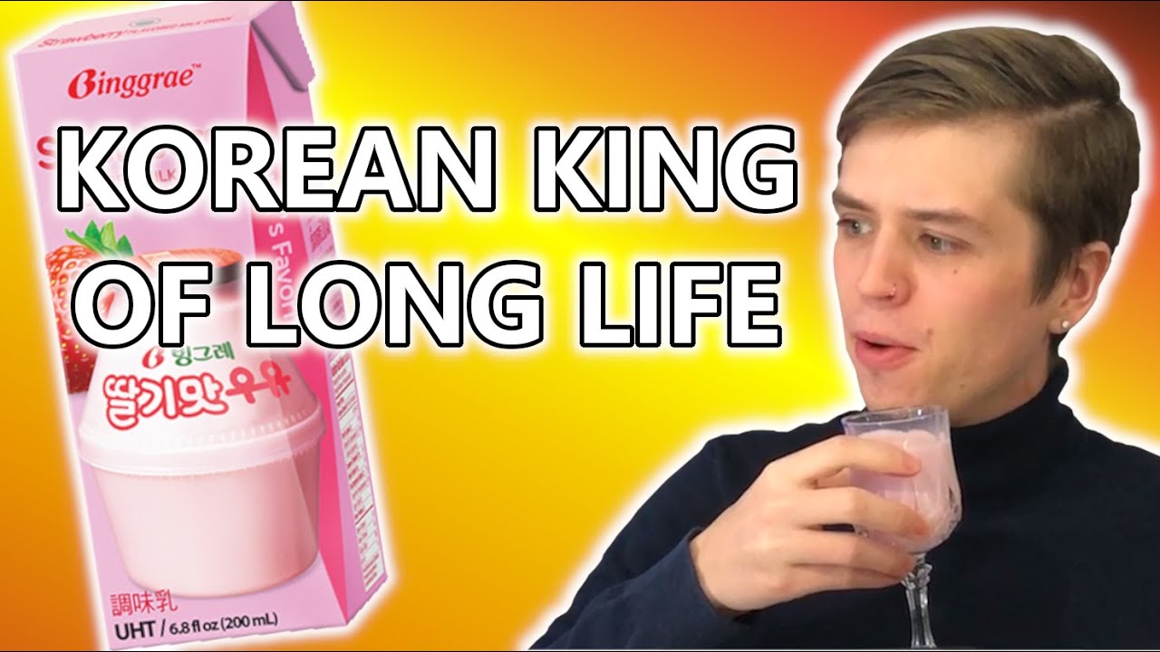 A pink Binggrae Korean strawberry milk bottle held in front of a Korean convenience store cold drinks section for a flavor review