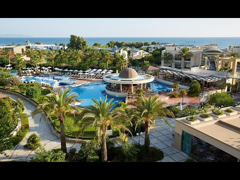 Außenansicht des Minoa Palace Resort & Spa mit Swimmingpool, Liegestühlen und Sonnenschirmen.