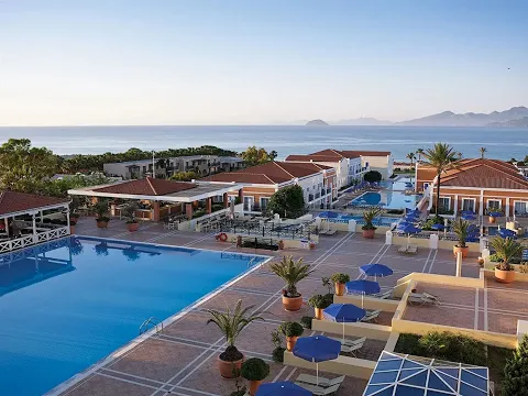 Luftaufnahme des Porto Bello Royal Hotels mit mehreren Swimmingpools und Bergpanorama im Hintergrund.