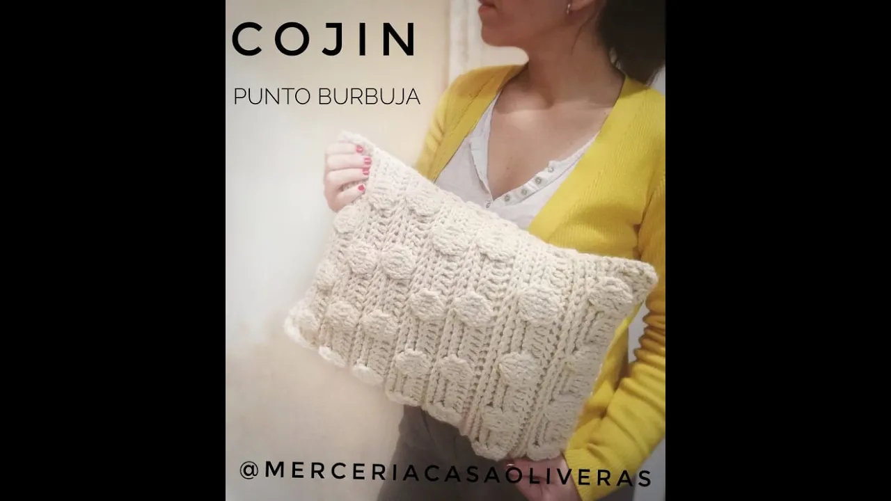Cojín de crochet color crema con franjas verticales en punto burbuja y arroz, sostenido por Soy Vane.