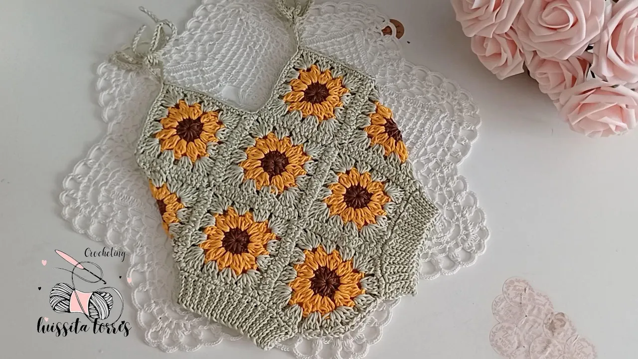 Body de bebé a crochet con grannys de girasol amarillo, centros marrones y bordes verde claro.