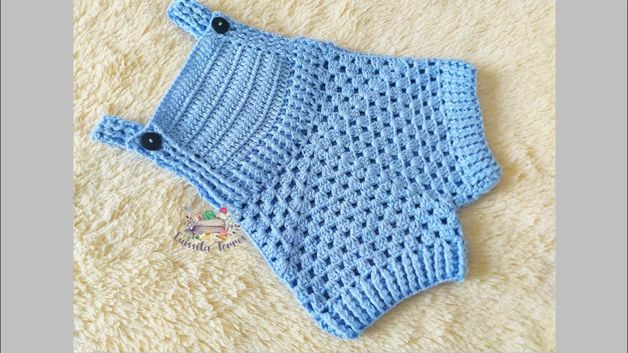 Overol azul de bebé a crochet con pechera tupida, cuerpo formado por dos grannys, perneras cortas y tirantes abotonados.