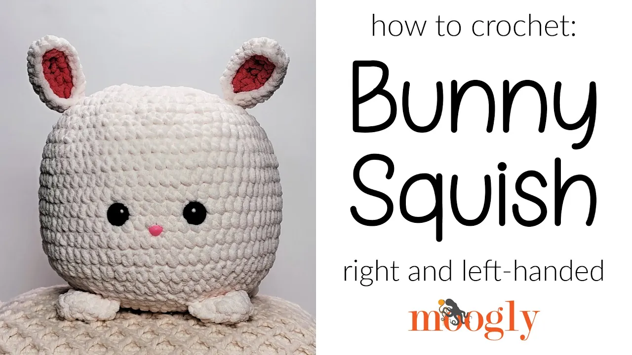 Cojín de conejo Bunny Squish a crochet blanco, de cuerpo redondo, orejas rosadas, ojos negros y cuatro patitas.